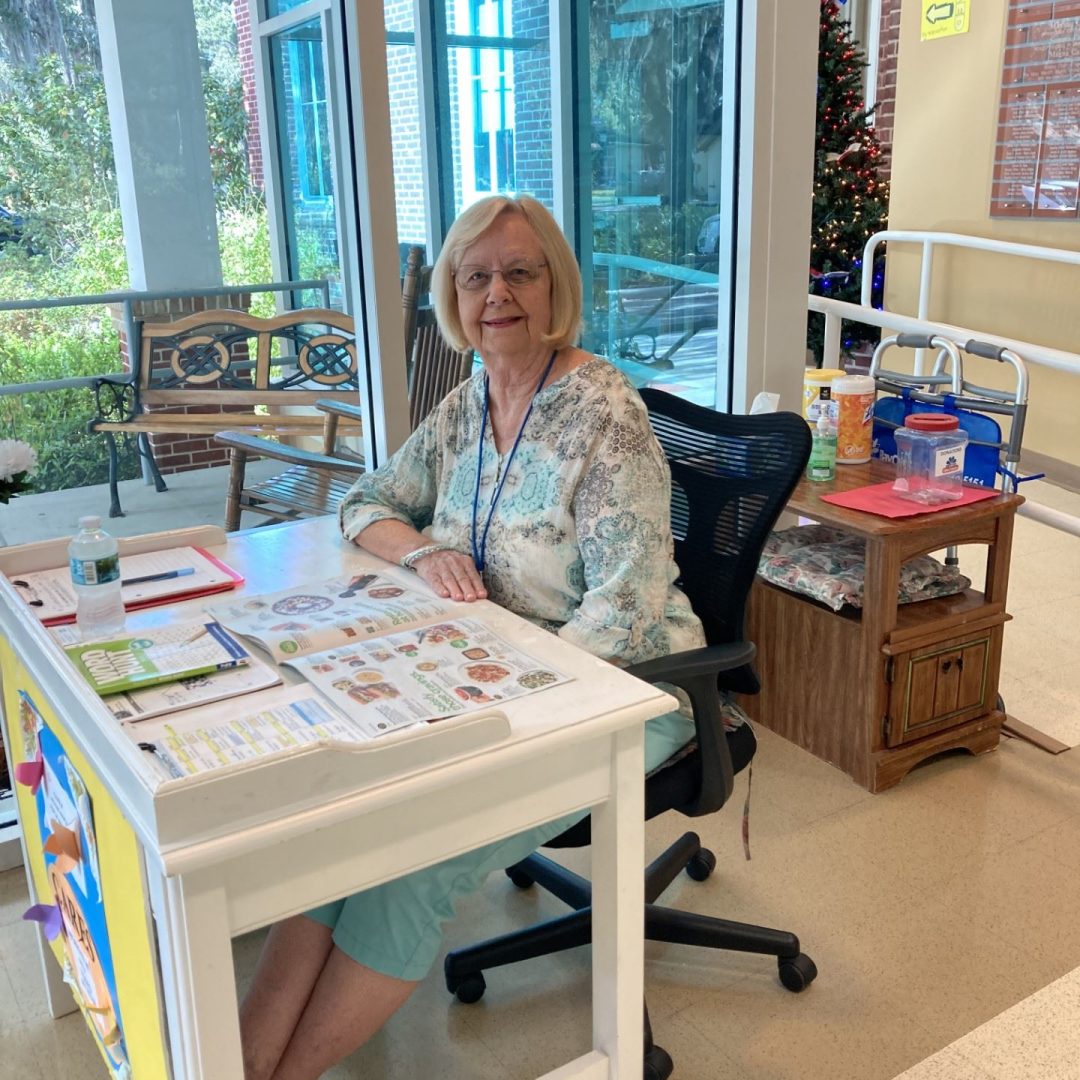 AmeriCorps Seniors RSVP volunteer with Seniors in Service sits at front desk and welcomes seniors at a senior center.