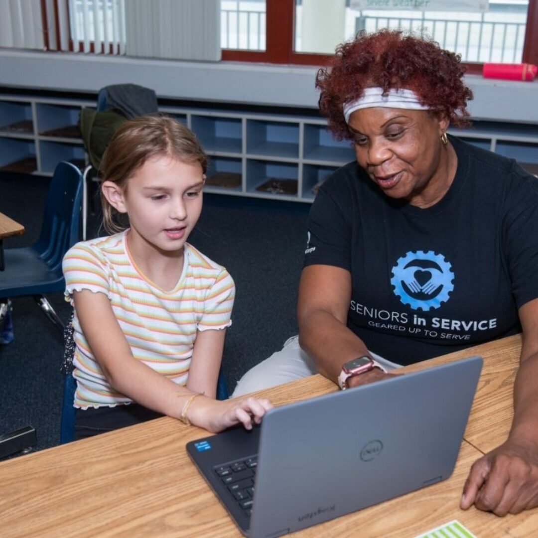 Classroom Grandparent Tutors Student on Letter Recognition on Laptop Classroom Grandparent volunteer tutors a student using a computer to practice letter recognition and phonics skills.