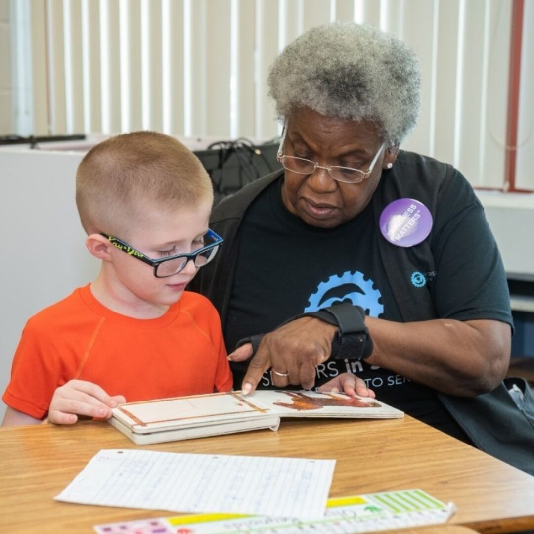 Classroom Grandparent Volunteer Helps Student With Sight Words Seniors in Service Classroom Grandparent volunteer helping student learning sight words with book.