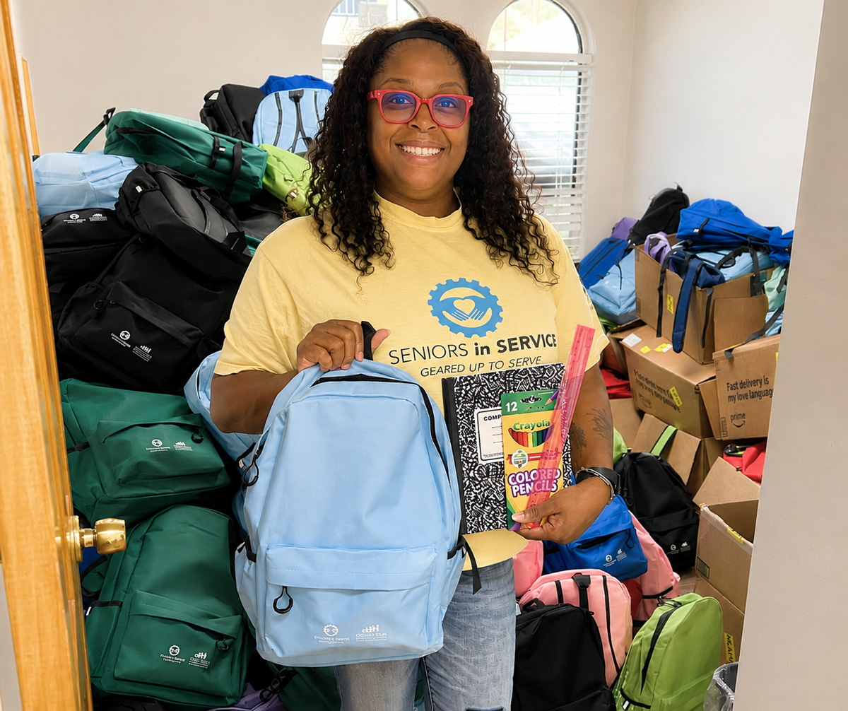 Seniors in Service volunteer holding a backpack and school supplies during a backpack stuffing event for local students.