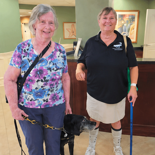 Support and Independence Through Community Two women stand with a guide dog during a Seniors in Service low-vision support group meeting at Lighthouse for the Blind & Low Vision.