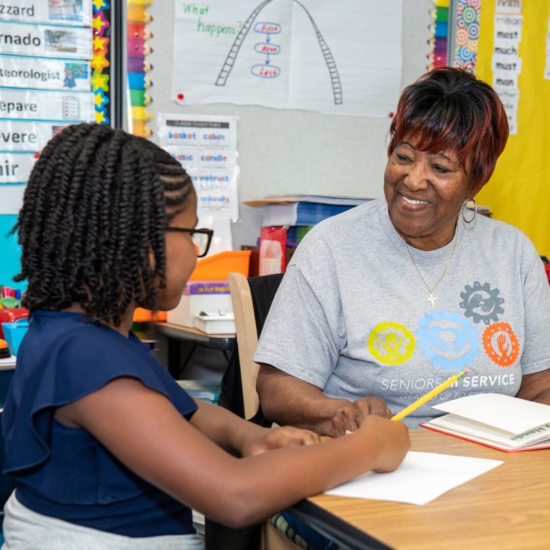 Classroom Grandparent Teaches Reading Comprehension Seniors in Service Classroom Grandparent volunteer smiling with student while teaching reading comprehension.