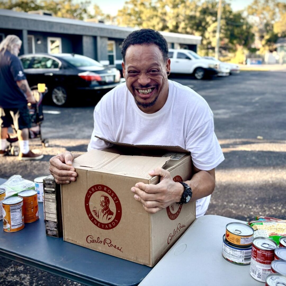 Veteran Excited To Receive Food From Mobile Pantry A veteran smiles while holding a box of packaged goods at a mobile food pantry.